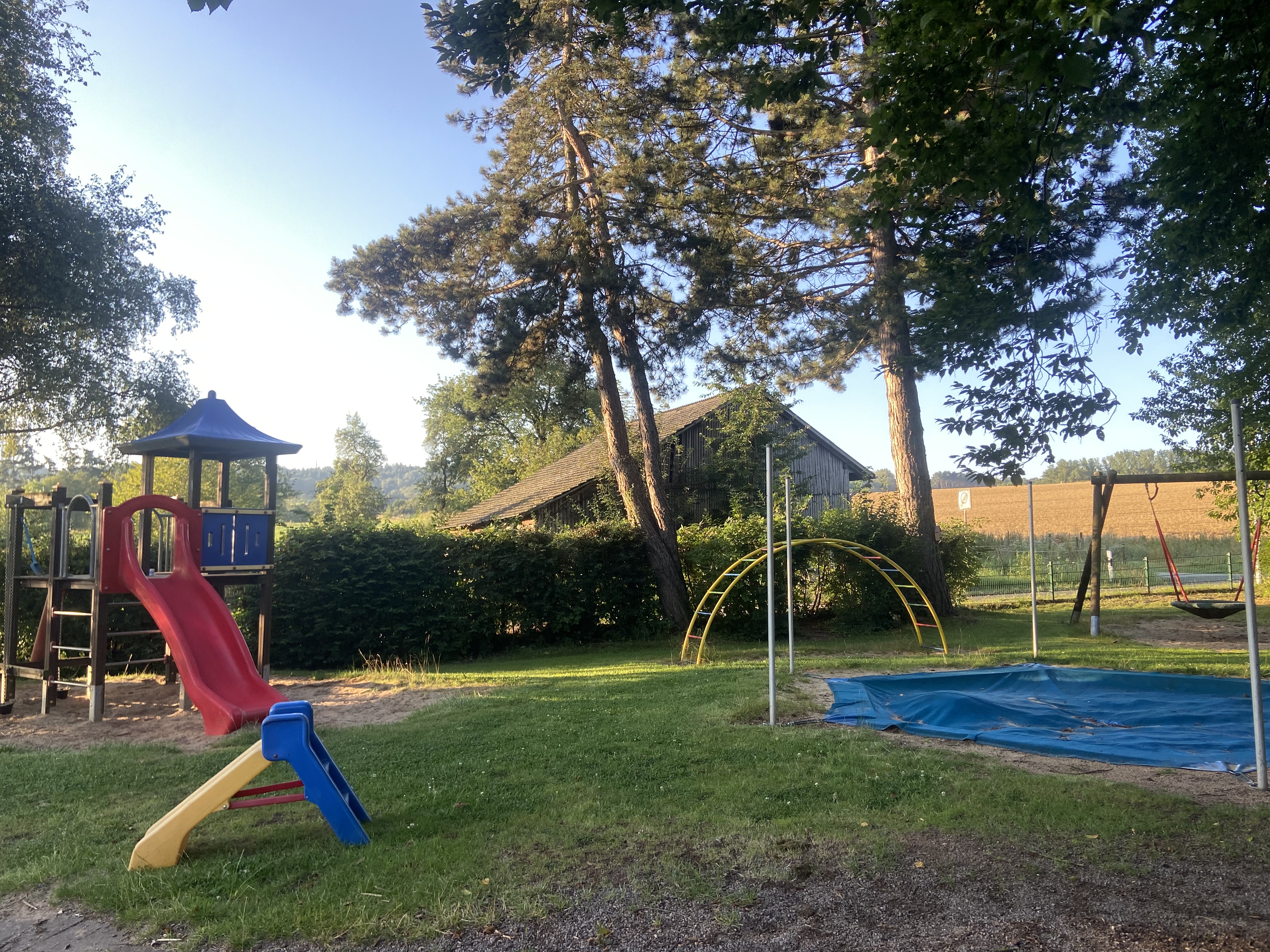 Auf dem Foto siehst du ein Stück des Spielplatzes mit Rutschen, Sandkasten, Nestschaukel und Klettergerüst