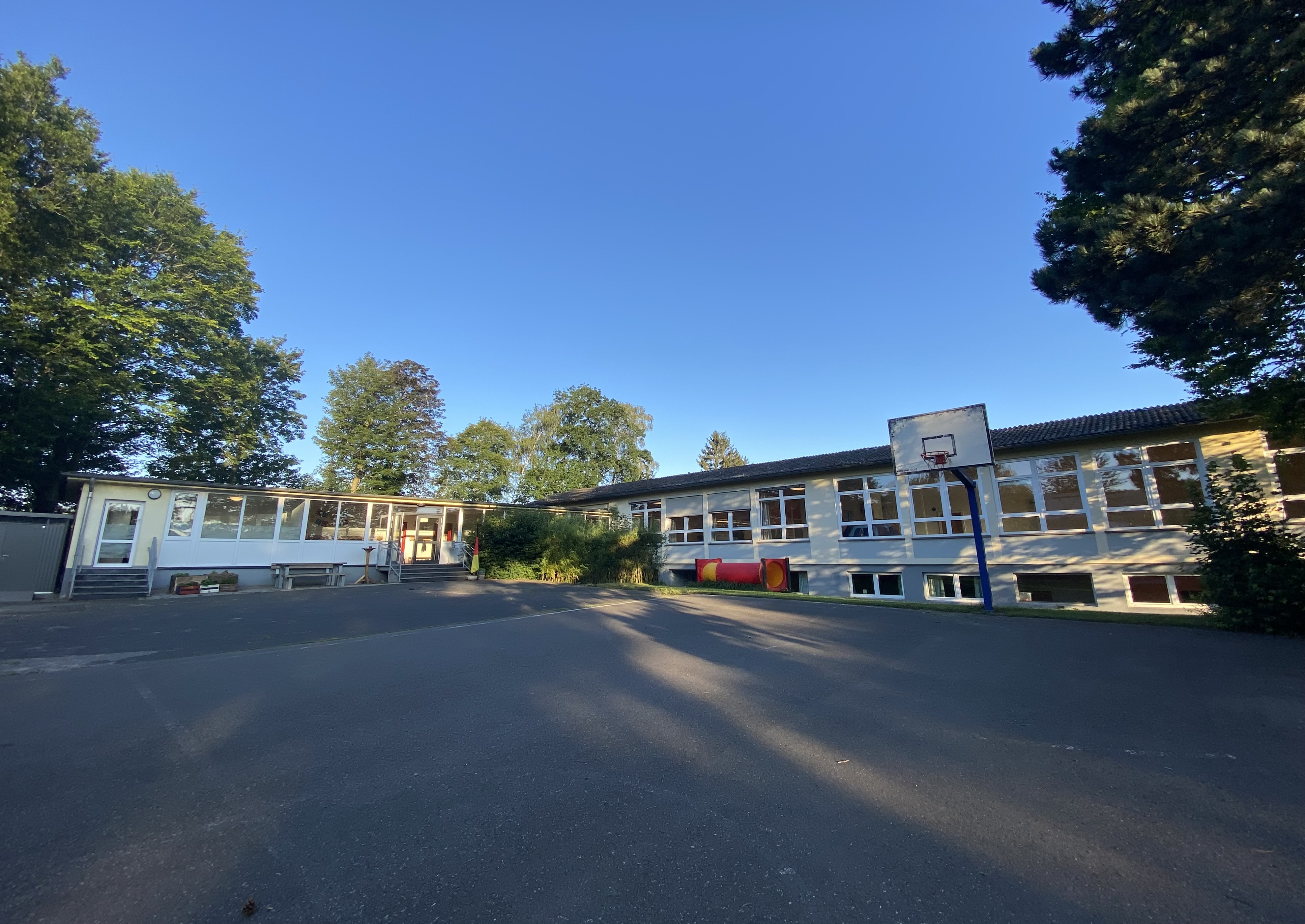 Auf dem Foto siehst Du das Kindergartengebäude und den großen Außenhof, auf dem die Kinder mit den Fahrzeugen fahren können.
